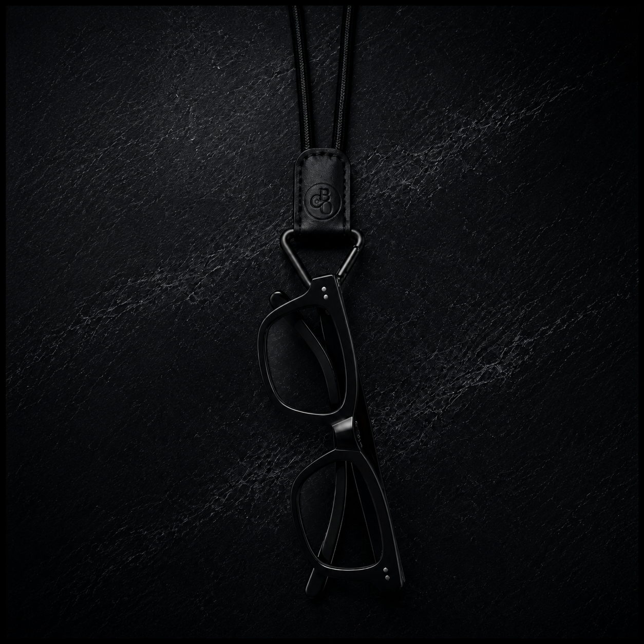 Black Signature Eyewear Necklace with glasses placed in the triangular Signature Loop on a dark textured background